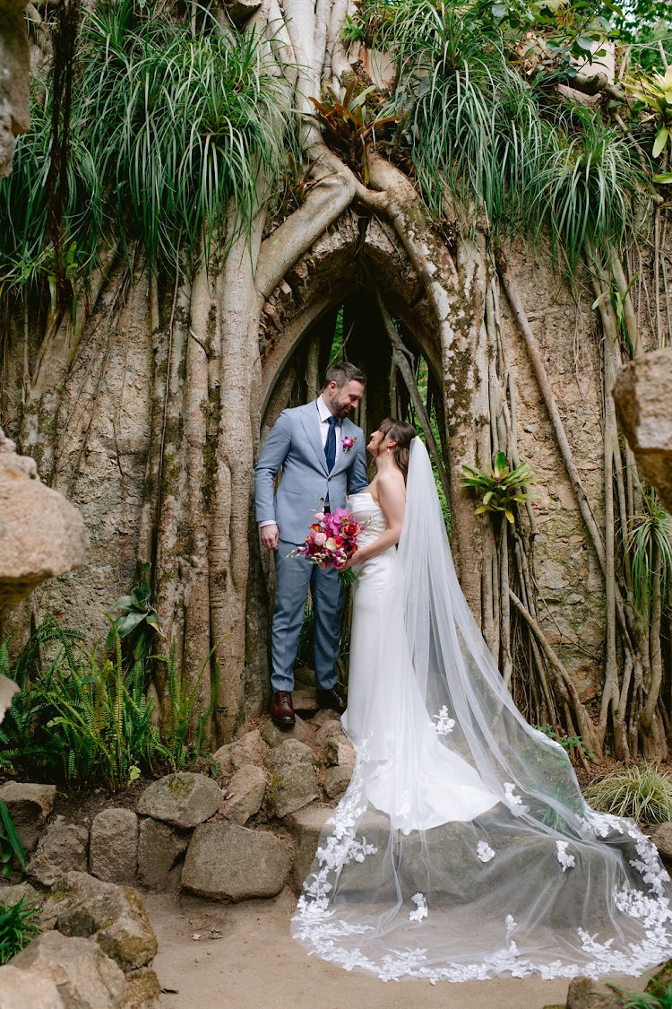 A groom and bride embracing in the fig-root archway of the Ruin Chapel at Monserrate Palace in Sintra, Portugal