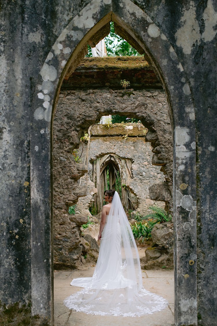 A bride in a long lace veil standing in the Gothic arches of the roofless Ruin Chapel at Monserrate Palace in Sintra, Portugal
