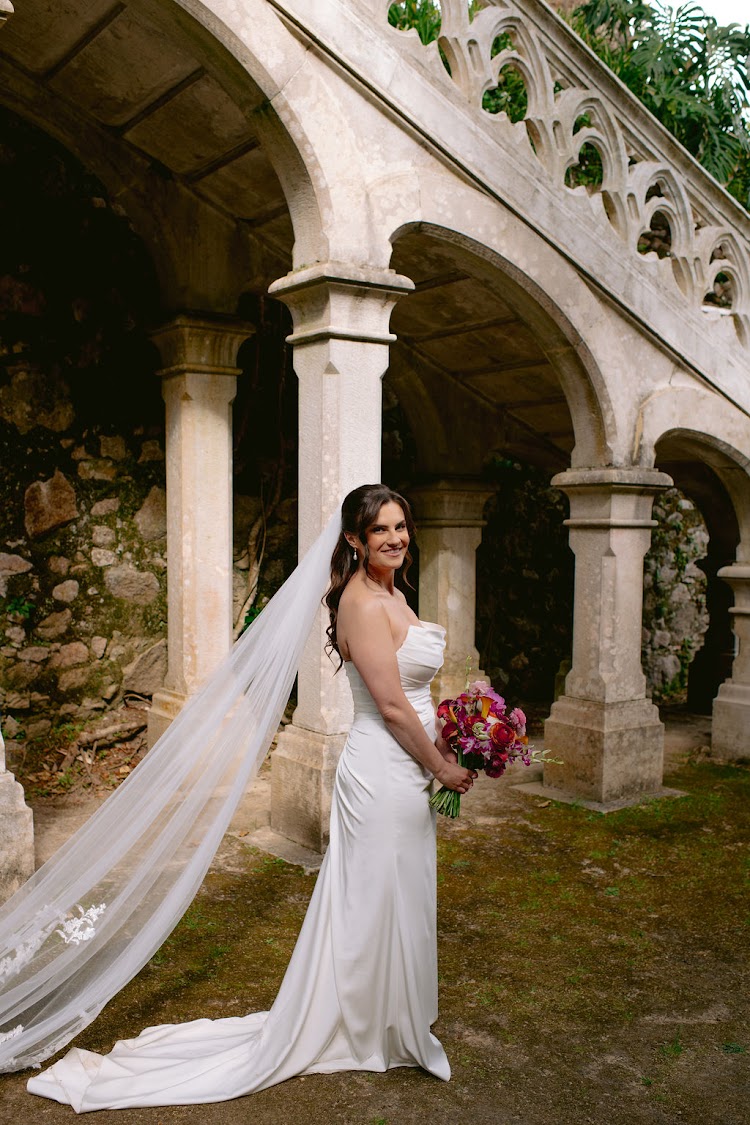 A smiling bride in a long veil in the stone arches of Monserrate Palace in Sintra, Portugal