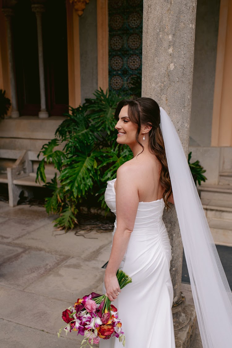 A bride with her bouquet in front of the ruined stone walls at Monserrate Palace in Sintra, Portugal