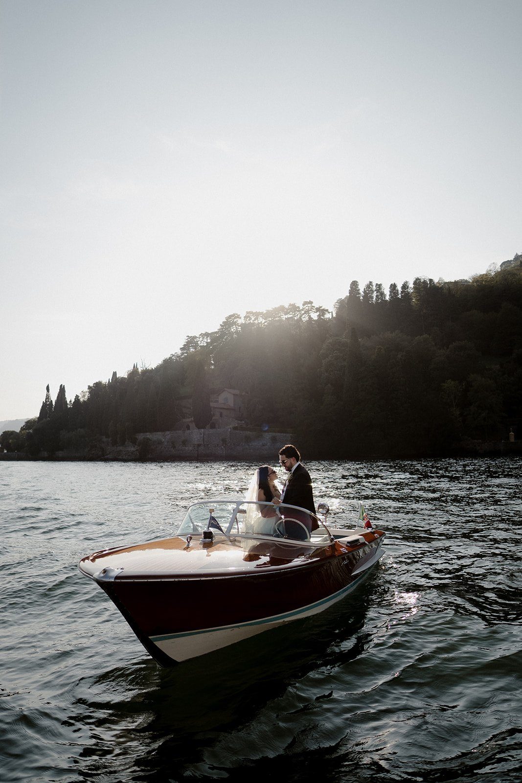 A couple on a vintage wooden boat on Lake Como, seen from behind in the evening light