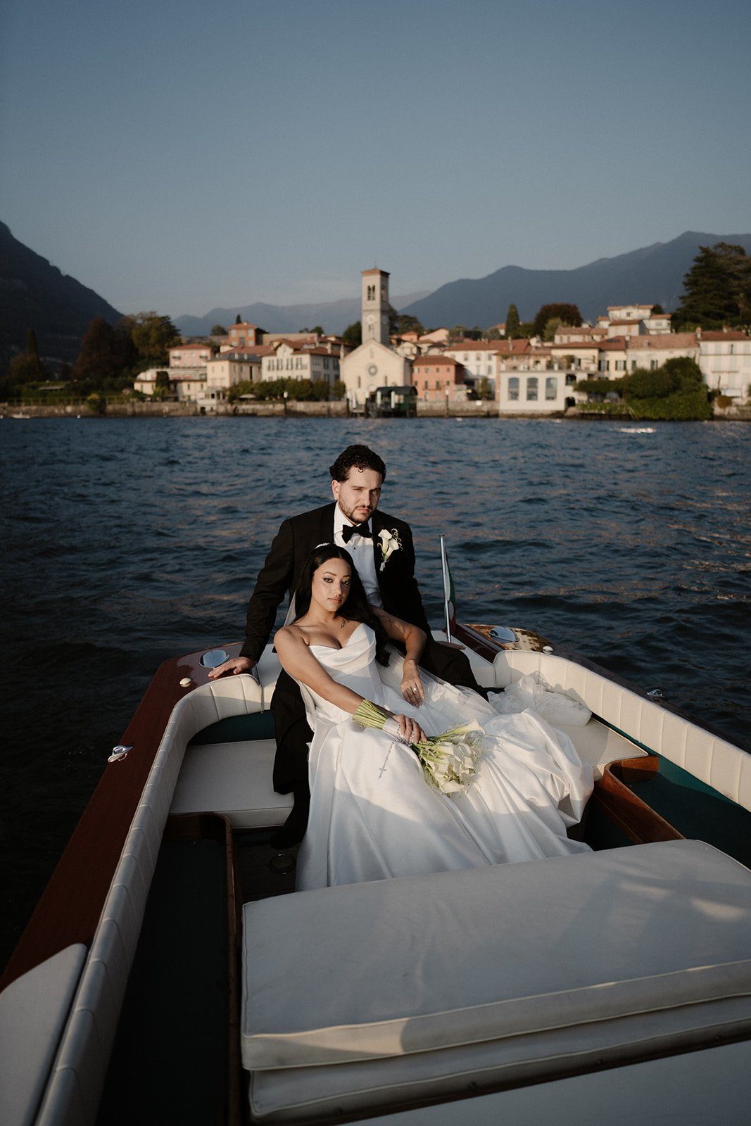 A couple relaxing on the cushions of a wooden boat, with a lakeside village behind