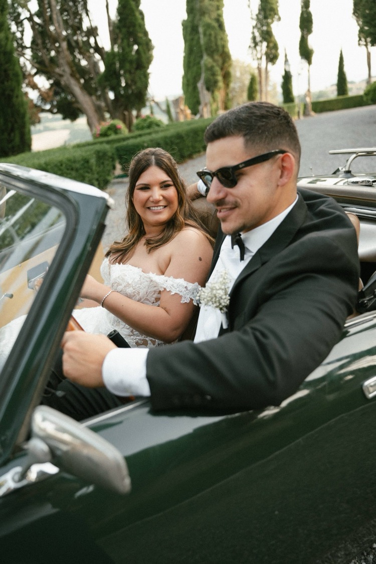 A smiling bride and groom riding in a vintage convertible at Villa Poggiano, Tuscany