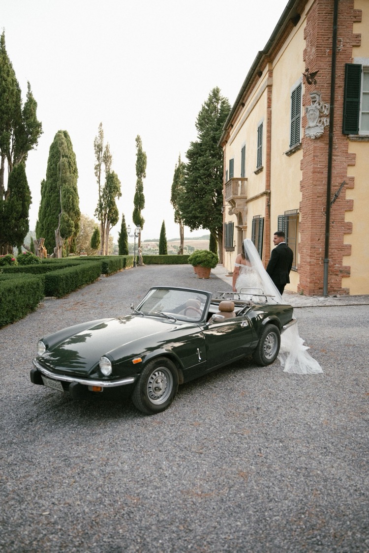 A vintage green convertible parked in front of the villa at Villa Poggiano in Tuscany, with the couple walking behind