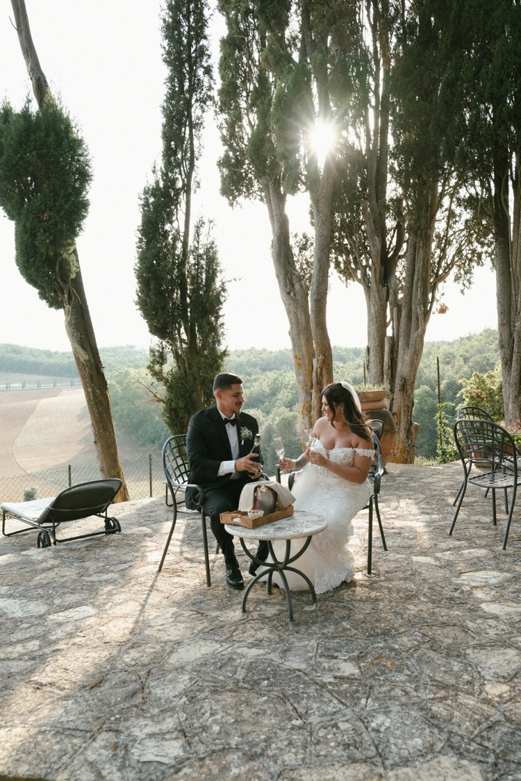A couple sharing a quiet moment at a table on the sunlit terrace at Villa Poggiano, Tuscany, with hills in the distance