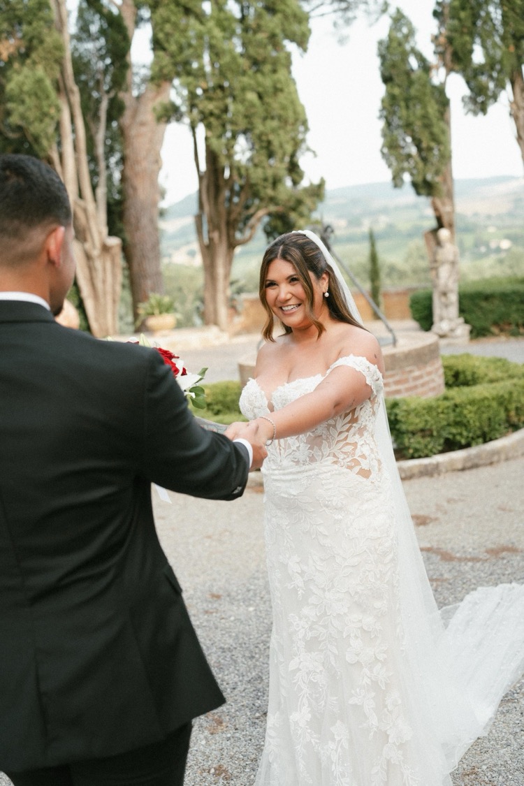 A groom taking his bride's hands in the garden at Villa Poggiano, Tuscany, as she laughs