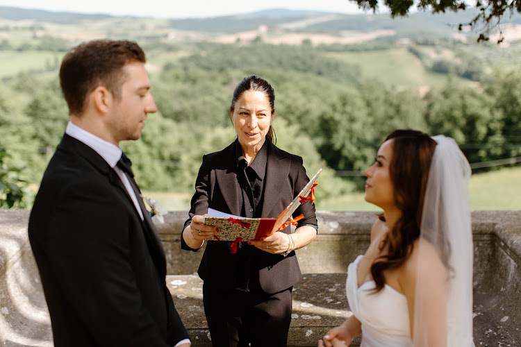 A groom and bride listening to the officiant during their ceremony at Villa Poggiano, Tuscany, with green hills behind