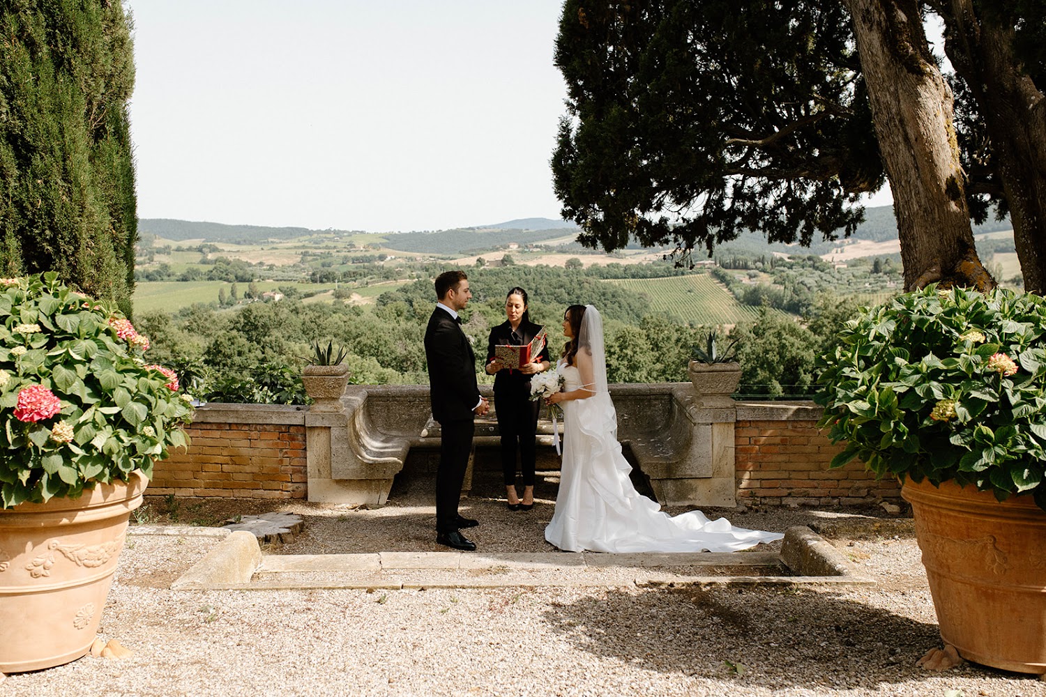 A couple exchanging vows on the garden terrace at Villa Poggiano, Tuscany, with rolling countryside views behind