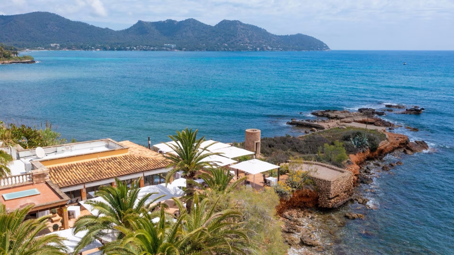 Restaurant Sa Punta on its rocky point above the sea in Mallorca, with the bay and mountains beyond
