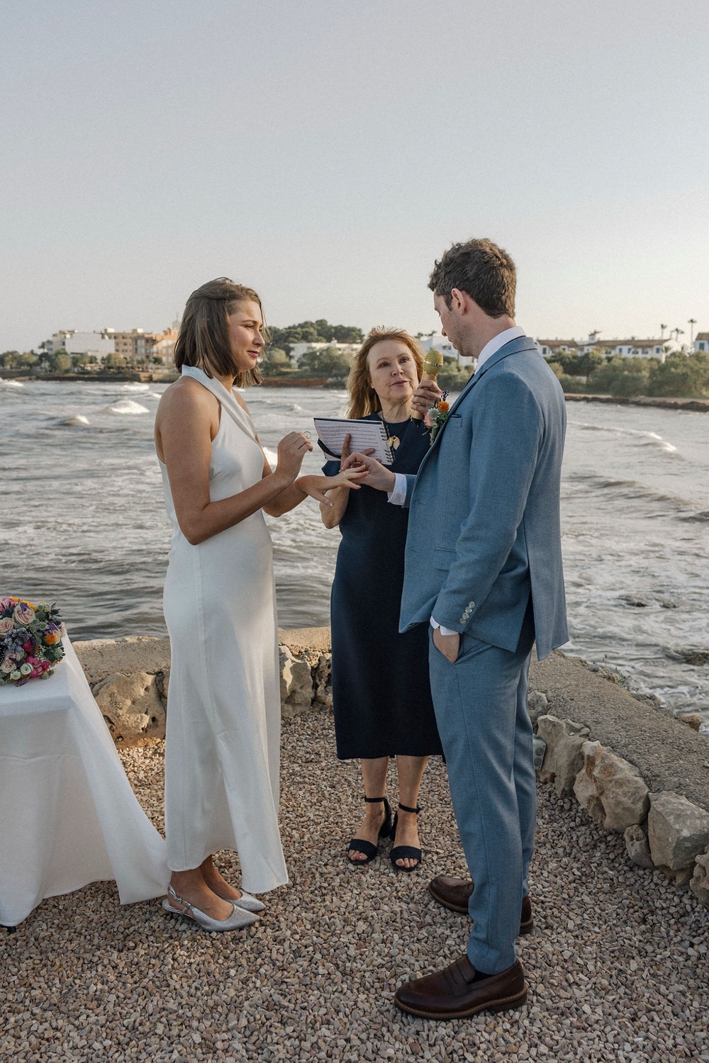 A couple exchanging vows with their celebrant at the mirador of Restaurant Sa Punta in Mallorca, with the sea behind them