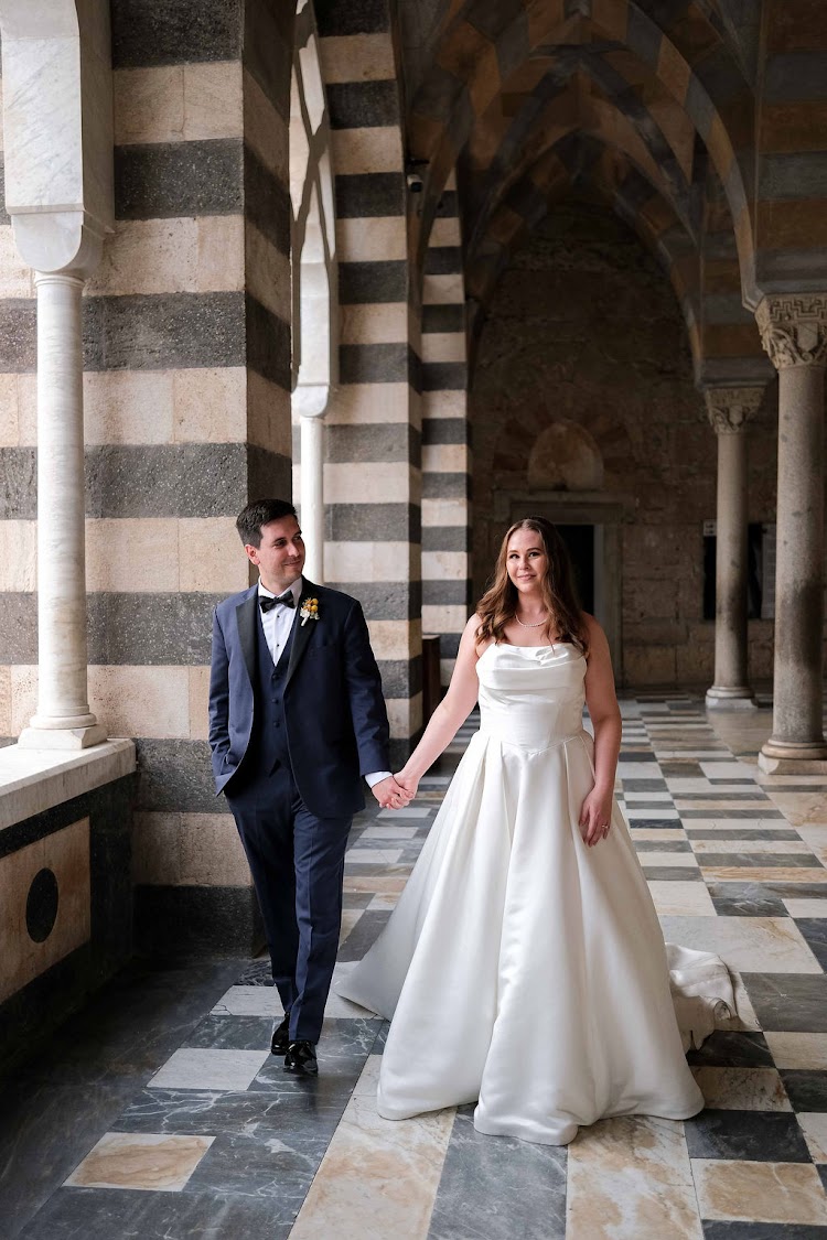 Couple walking hand in hand through the striped arcade of Amalfi Cathedral in Amalfi, Italy