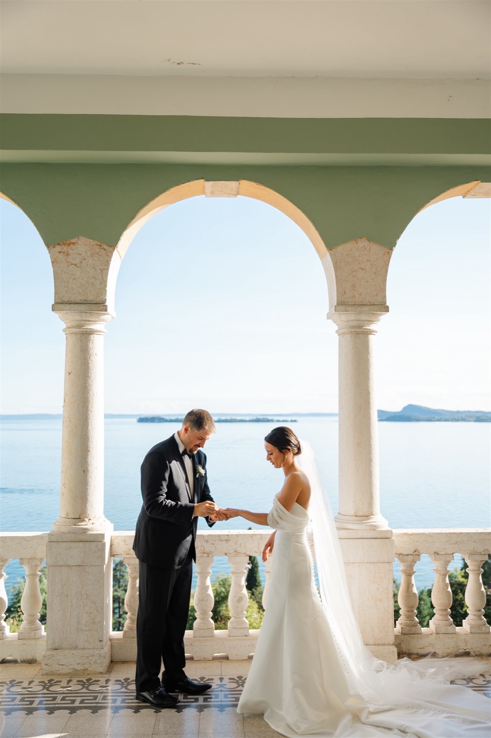 A groom putting the ring on his bride's finger under the arches of the terrace at Villa del Sogno on Lake Garda