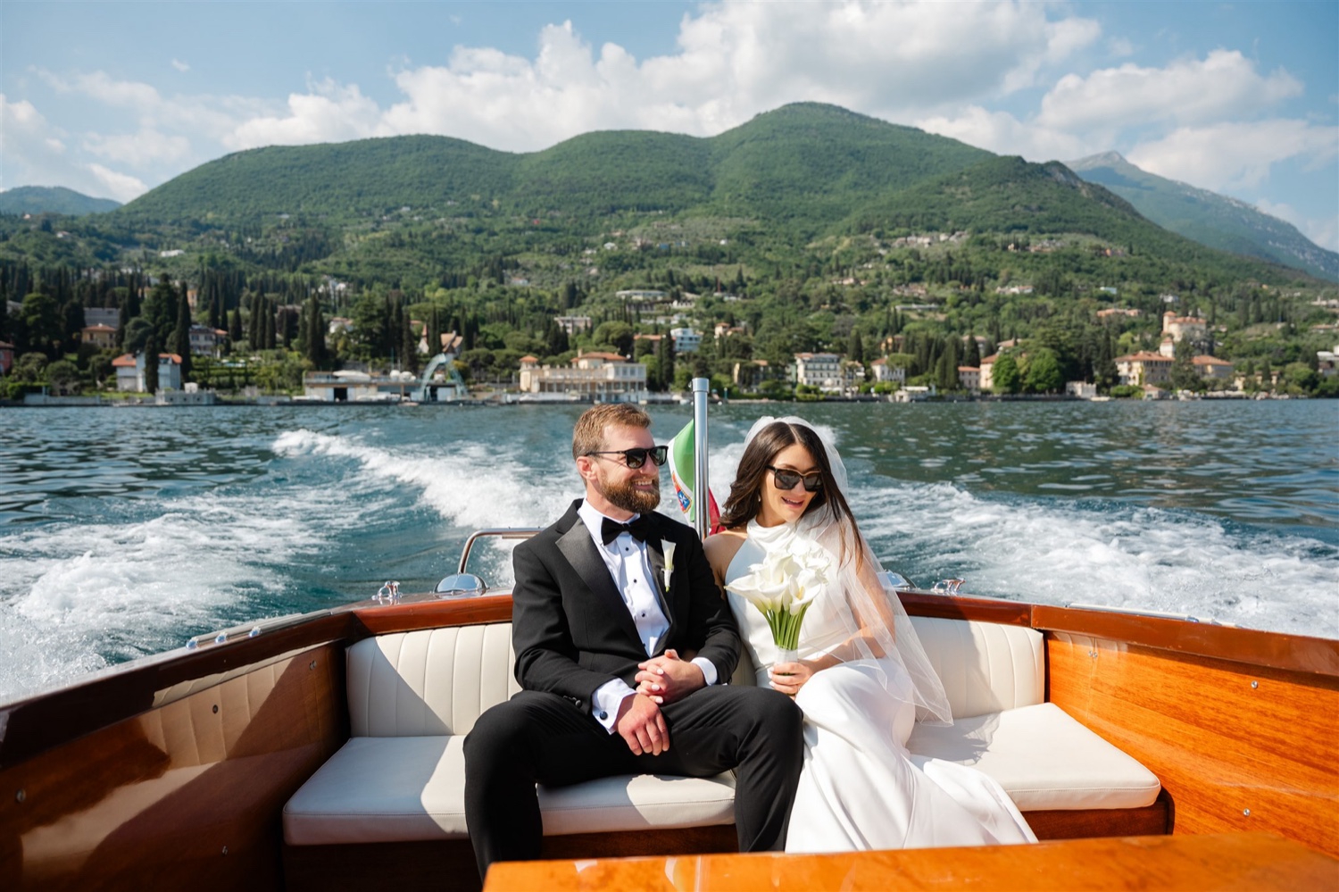 A couple in sunglasses sitting in a classic wooden boat on Lake Garda