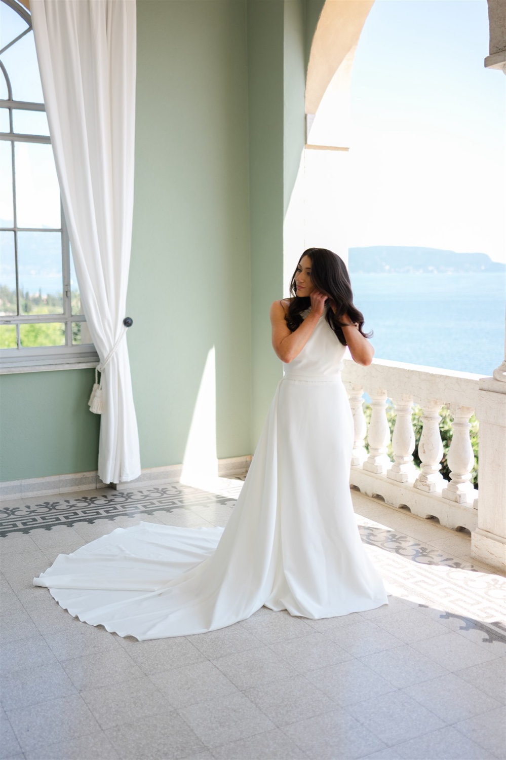 A bride adjusting her earring on the terrace of Villa del Sogno on Lake Garda, with the lake behind her