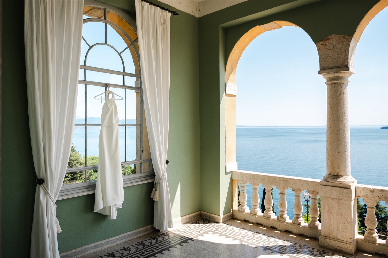 A wedding dress hanging in the window of the suite terrace at Villa del Sogno on Lake Garda, with the lake beyond