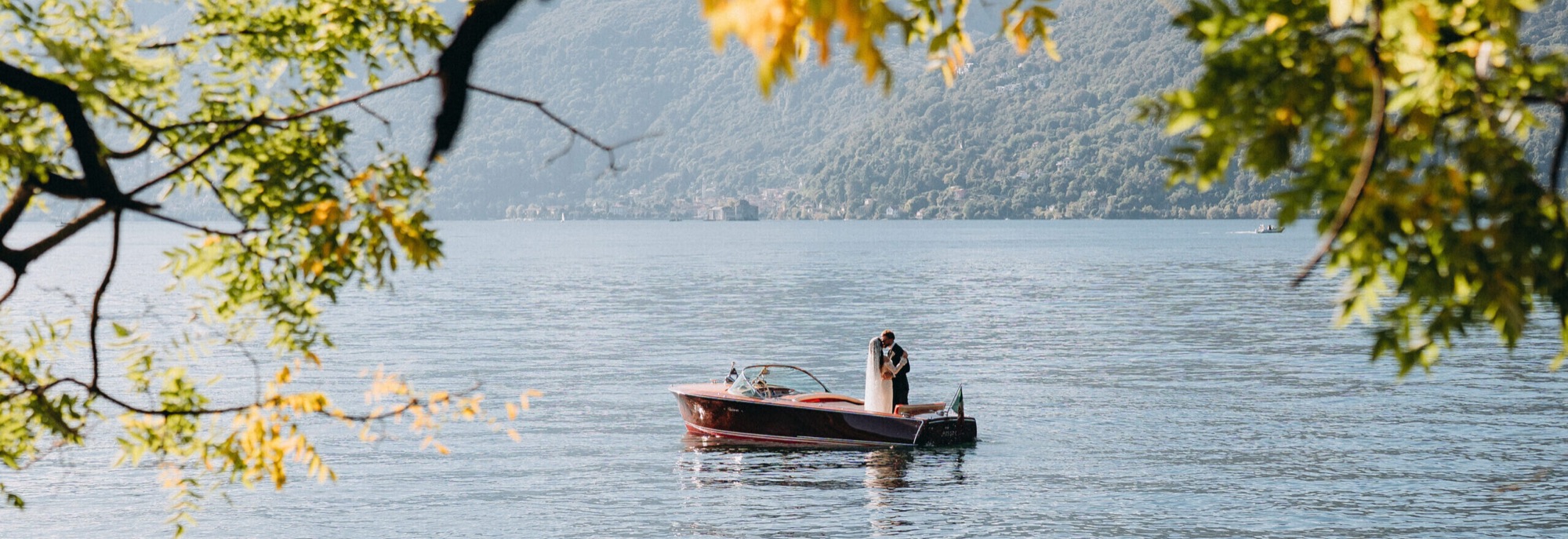 A couple kissing on a classic wooden boat on the calm water of Lake Maggiore, Italy
