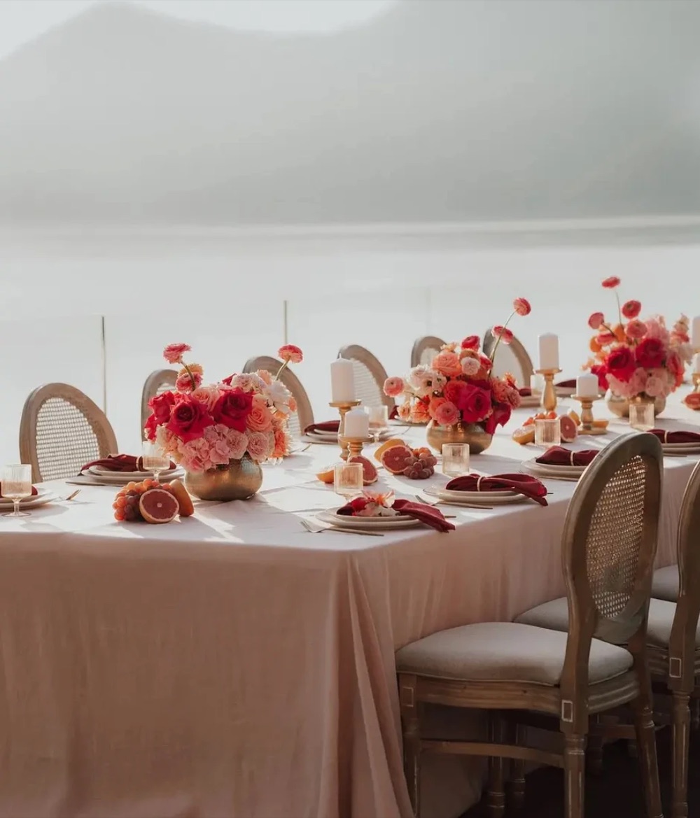 A long table set with pink linen, red roses and grapefruit centrepieces on the lakeside terrace of Villa Porta, Lake Maggiore, Italy