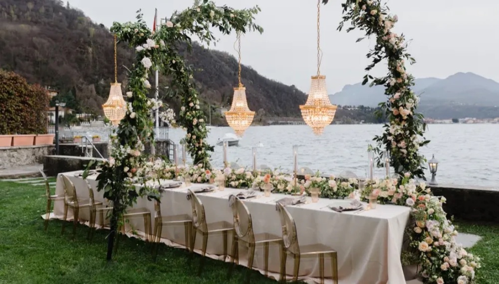 A garden dinner table with flower arches and crystal chandeliers beside the water at Villa Porta on Lake Maggiore