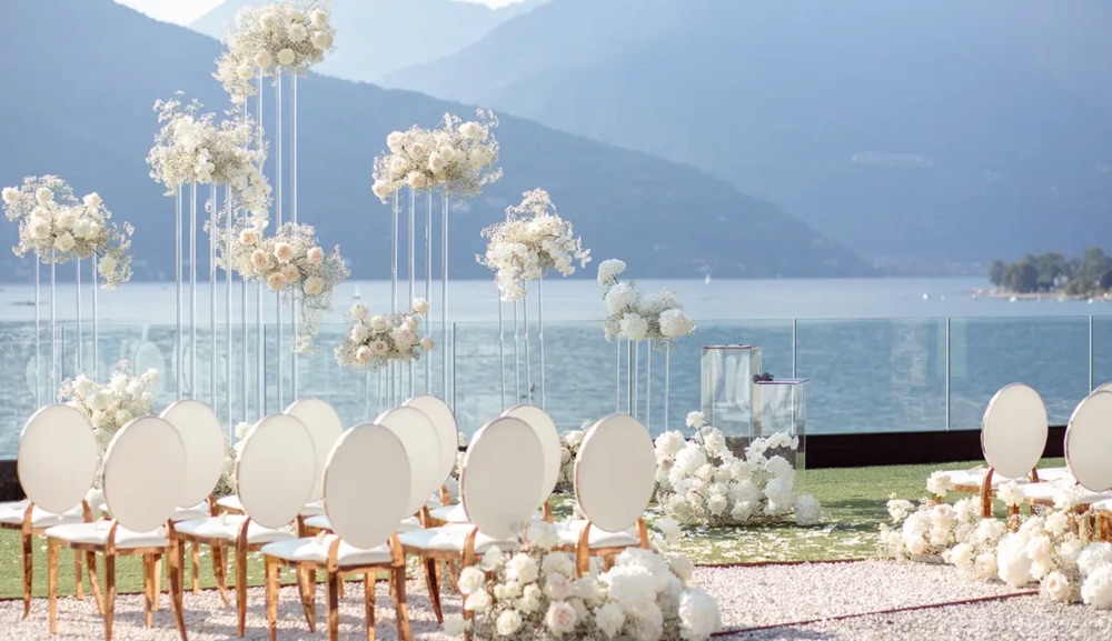 Tall white floral stands and rose gold chairs set for a ceremony beside the glass terrace at Villa Porta, Lake Maggiore, Italy