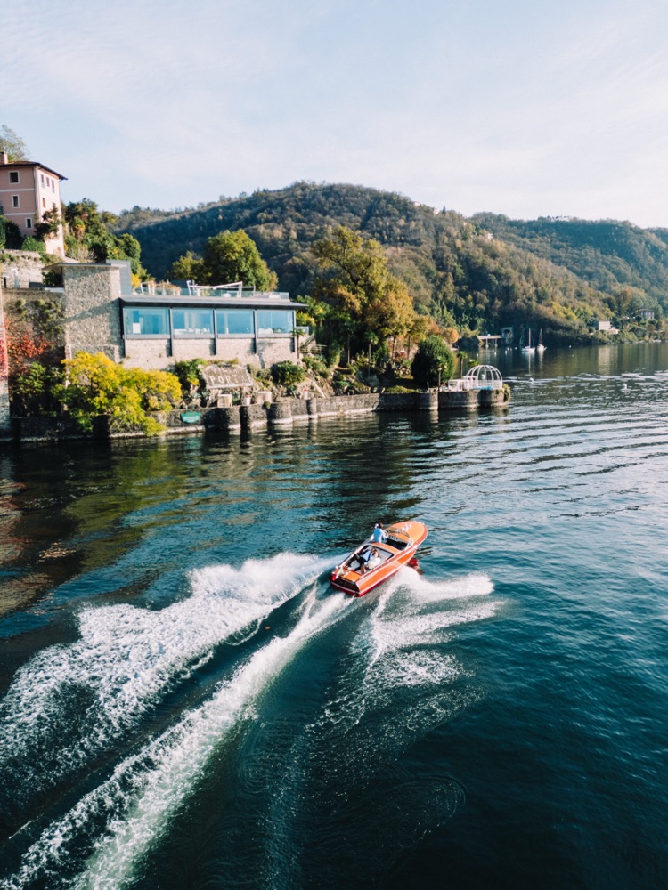 Aerial view of a speedboat on Lake Maggiore passing the lakeside villa and gardens of Villa Porta in Italy