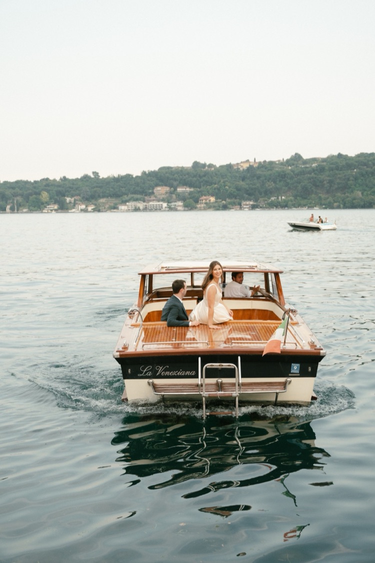 A smiling bride looking back from the stern of a vintage wooden boat on Lake Garda during her elopement in Italy
