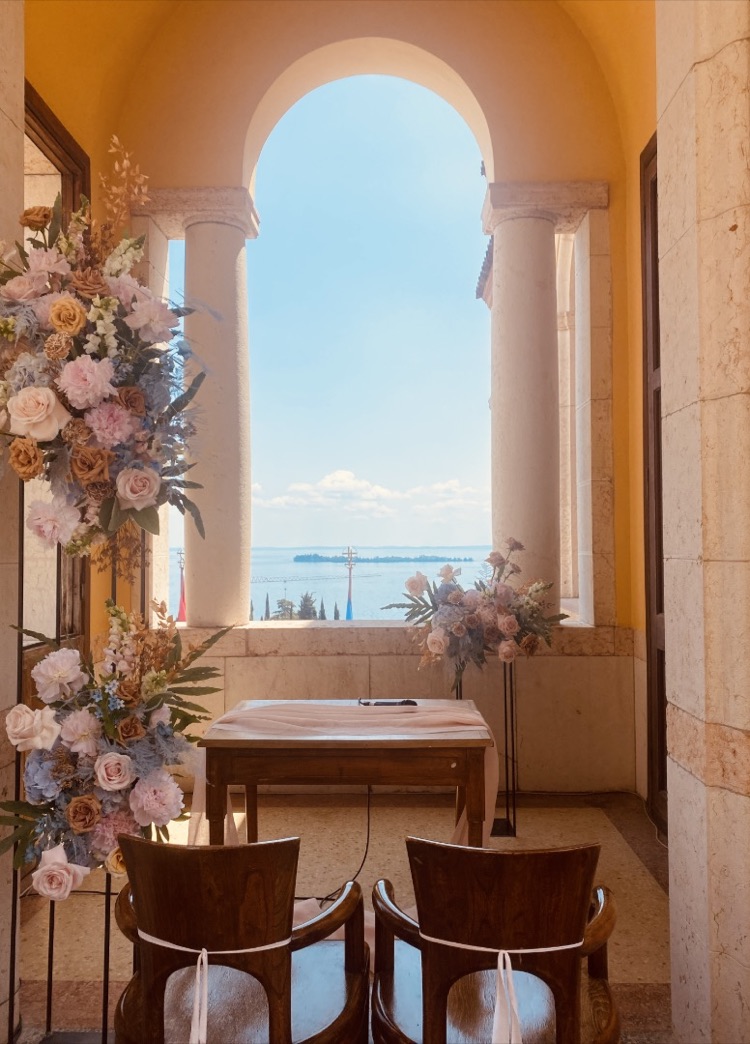Elopement ceremony setup with white chairs and soft pink flowers on the arched balcony of Il Vittoriale overlooking Lake Garda