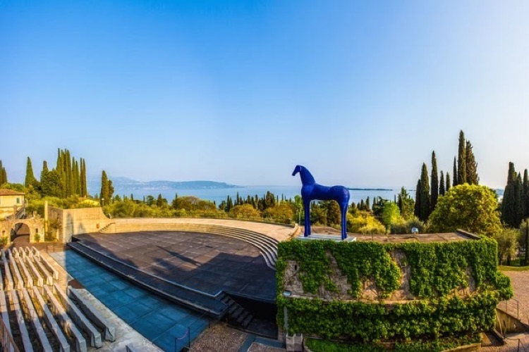 The amphitheatre and gardens of Il Vittoriale with a blue horse sculpture and Lake Garda in the distance