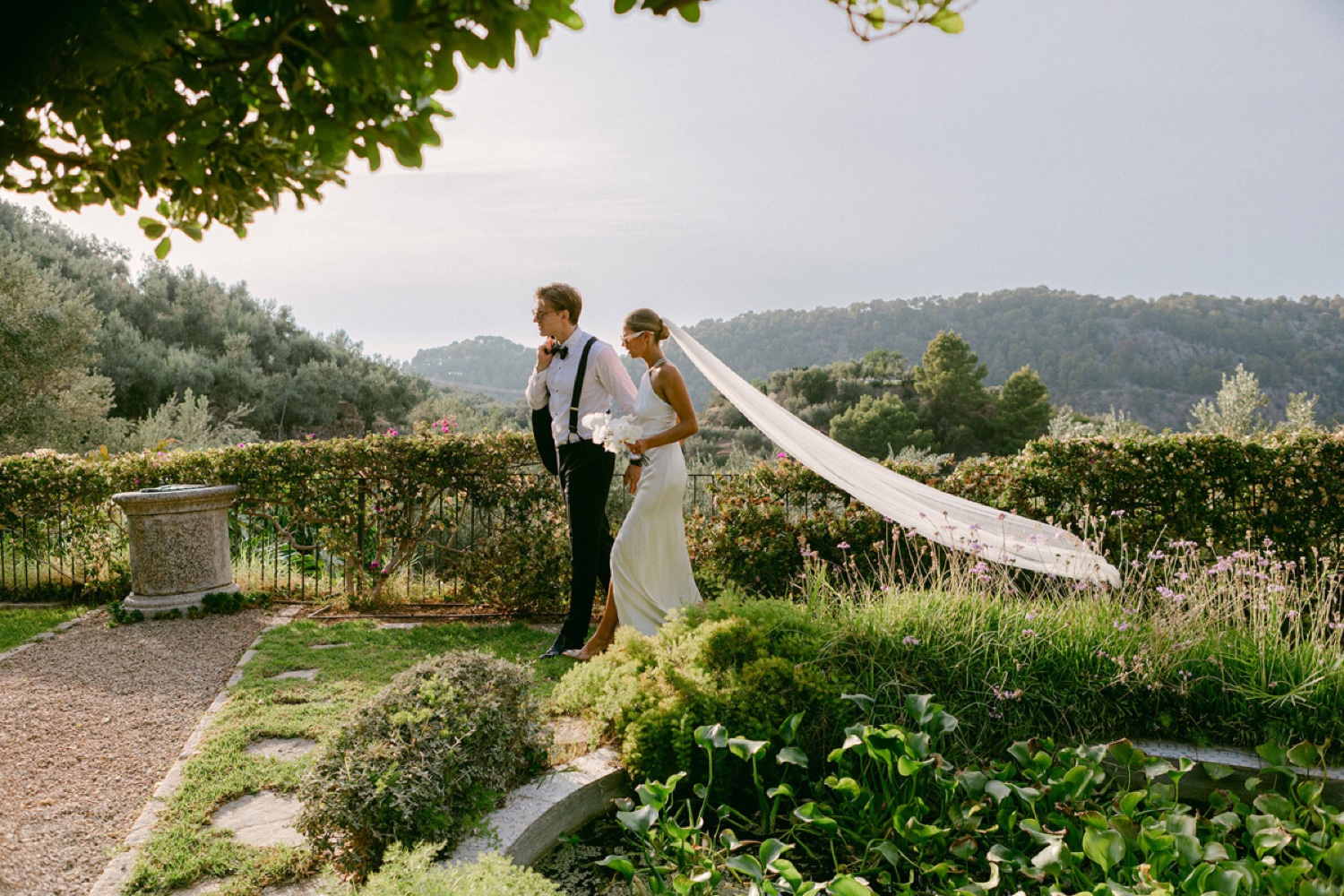 A couple walking through the gardens of Ca’s Xorc in Mallorca, with the bride’s long veil in the wind