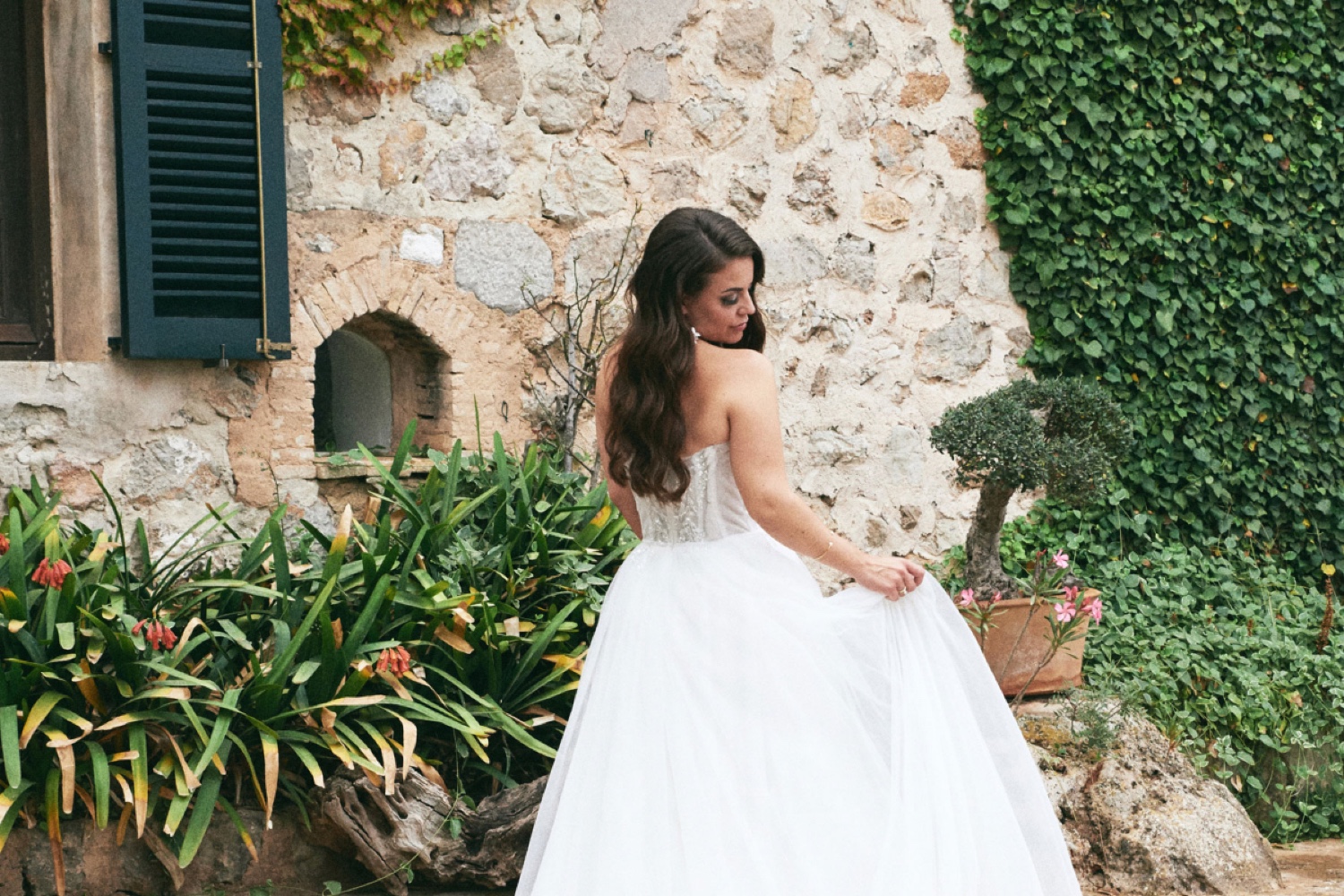 A bride holding her dress in front of the old stone wall of Ca’s Xorc in Mallorca