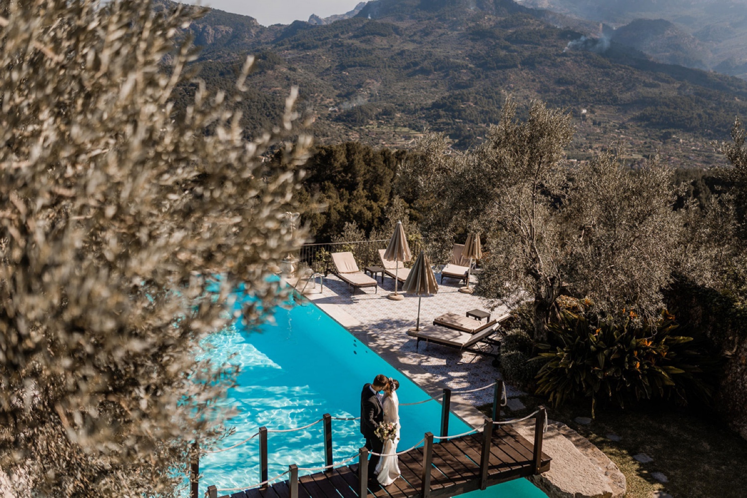 A couple embracing by the turquoise pool of Ca’s Xorc, with the mountains of Mallorca behind
