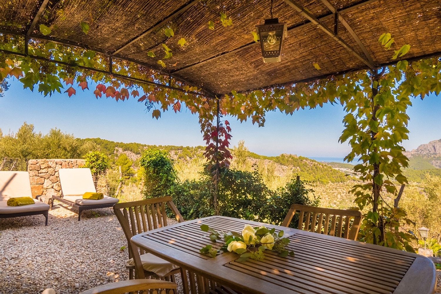 A pergola terrace with a wooden table at Ca’s Xorc in Mallorca, with the sea in the distance