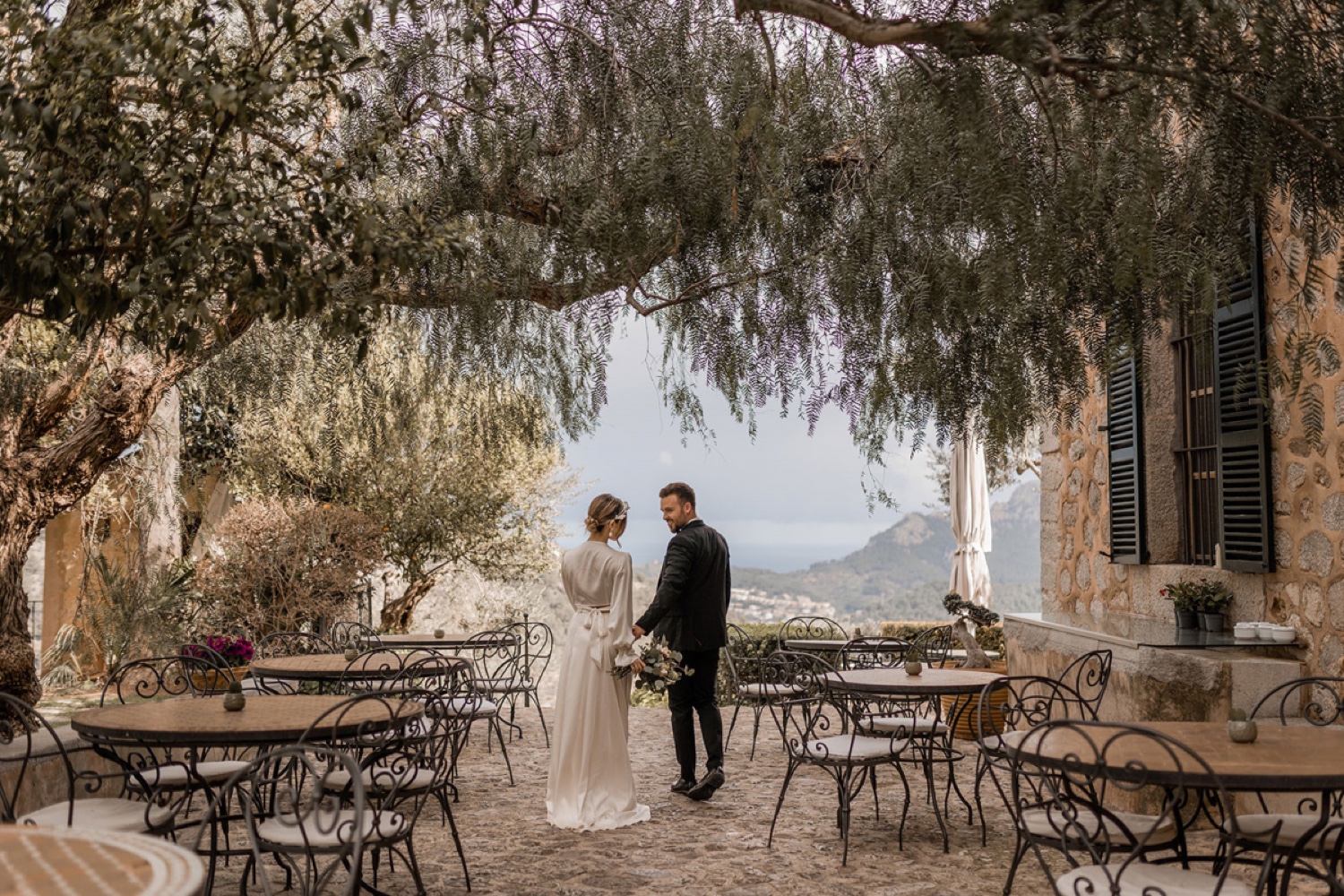 A couple standing under old olive trees on the terrace of Ca’s Xorc in Mallorca, with the valley behind them